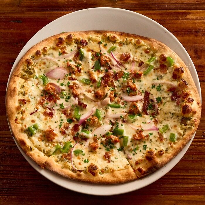 Bacon and sausage pizza on an alfredo pesto base with green peppers and red onion