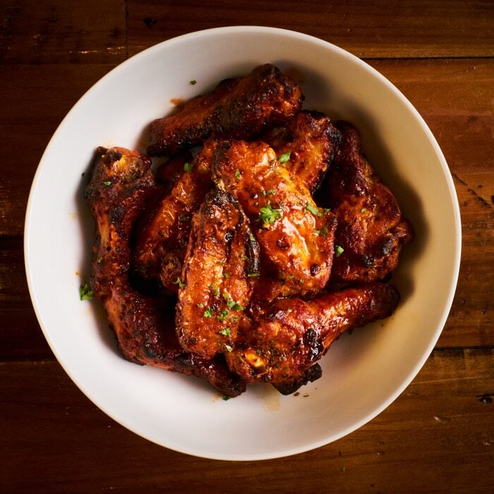 Bowl of oven-baked bone-in chicken wings tossed in sauce