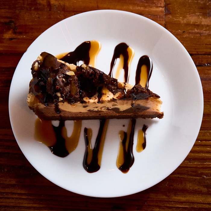 Gluten-free peanut butter fudge cheesecake on a flourless brownie base with chocolate drizzle