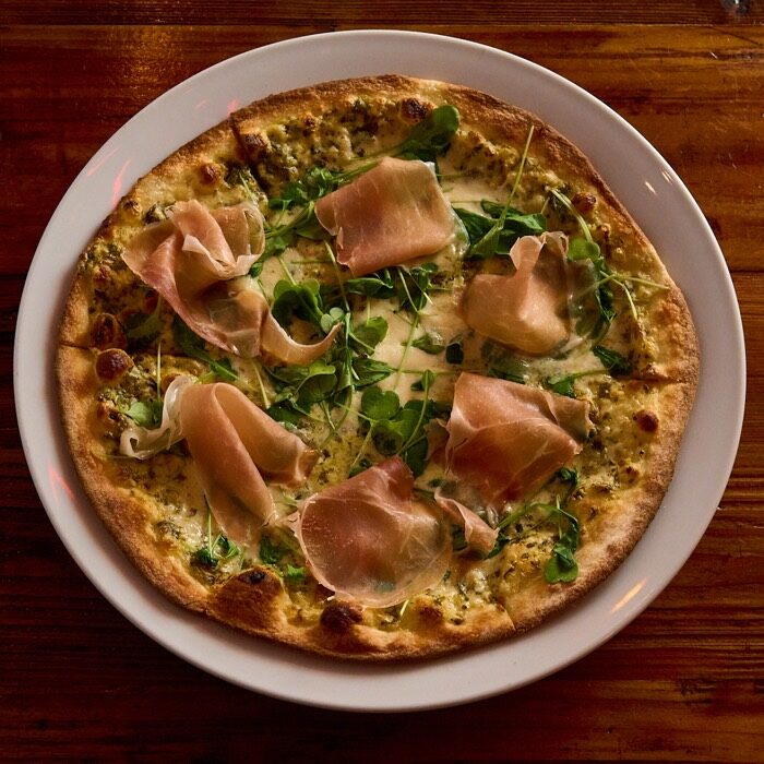 Prosciutto and arugula pizza on alfredo pesto with fresh mozzarella