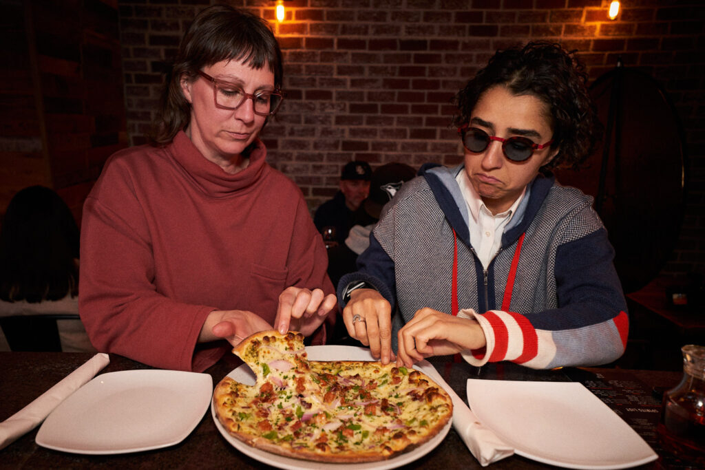 Two friends about to take a slice from a shared pizza at JZ's Pizza