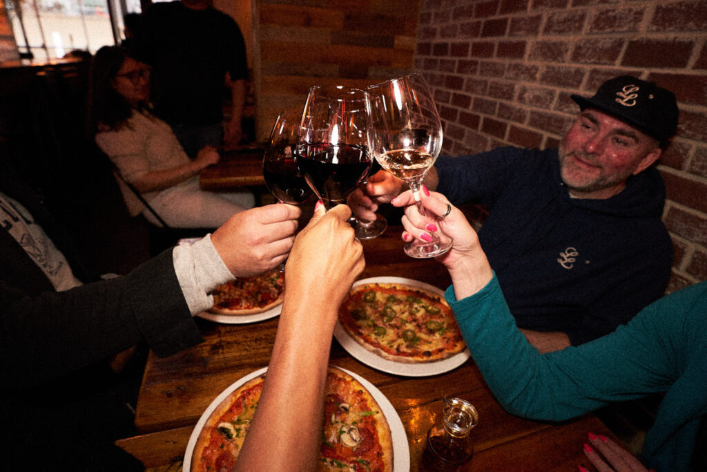 Guests clinking wine glasses over pizza at JZ's Pizza