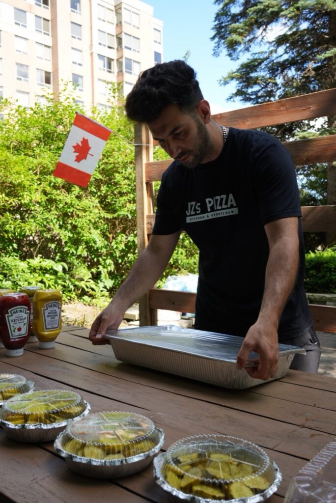 A JZ’s Pizza team member setting out catering trays and pickles at an outdoor BBQ