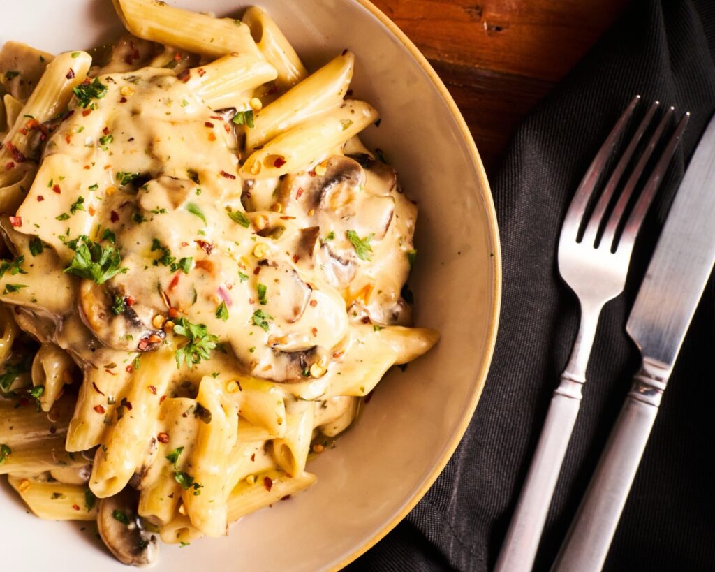 Chicken alfredo penne with mushrooms, parsley and chili flakes in a white bowl
